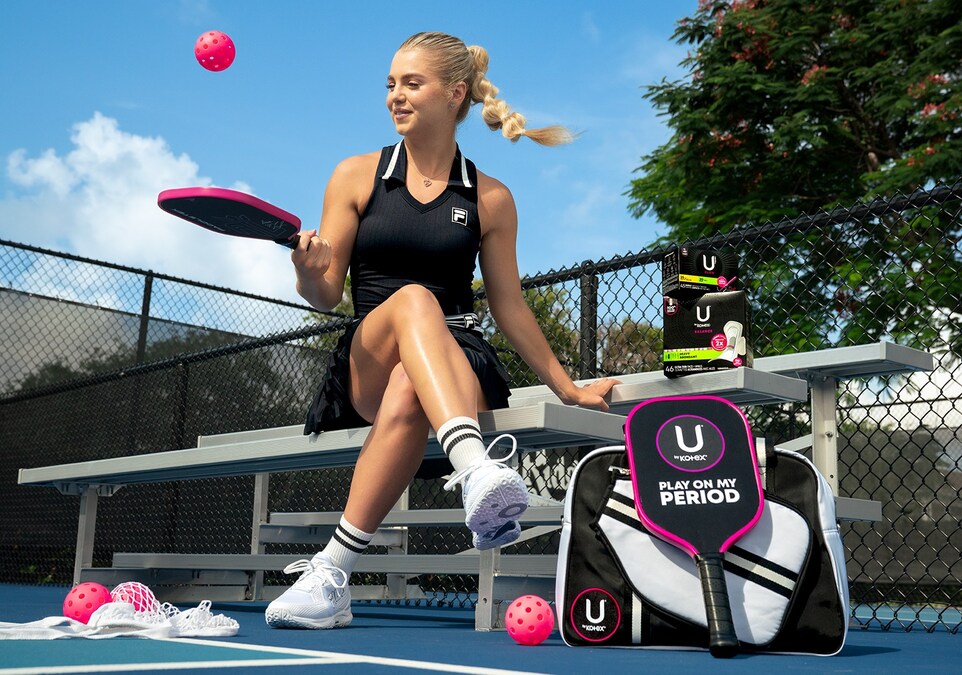 Anna Leigh Waters sitting on pickleball court bench holding paddle, Fila outfit, pink pickleball, and U by Kotex sponsorship gear.