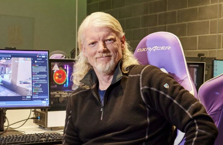 Twitch CEO Dan Clancy sitting in a gaming chair beside a computer setup with a live Twitch stream on screen.